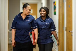 Two female Jane Lewis nurses in uniform walking down a service corridor holding folders