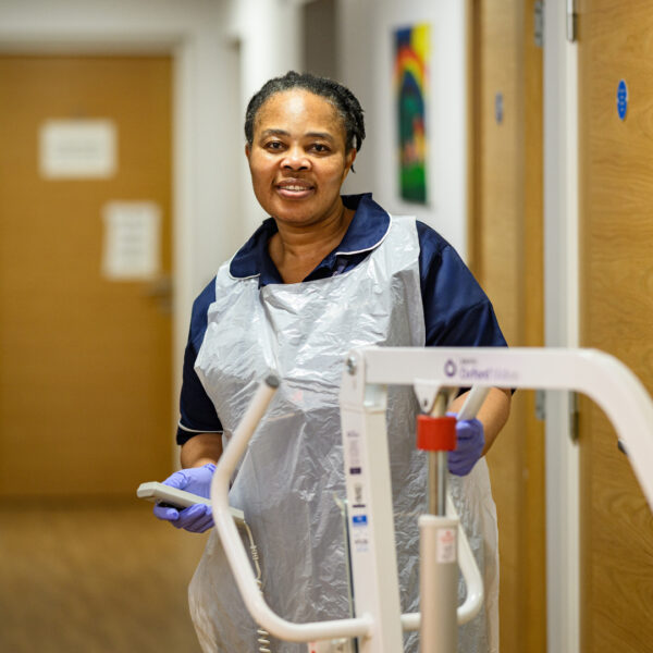 Female Jane Lewis Nurse in PPE moving a hoist in service corridor