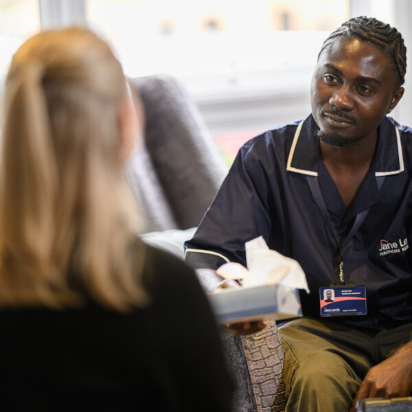 A male nurse in Jane Lewis uniform offering a female service user a tissue