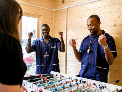 Two male Support Workers playing table football with service user
