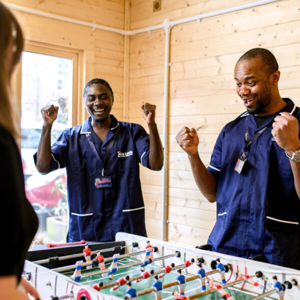 Two male Support Workers playing table football with service user
