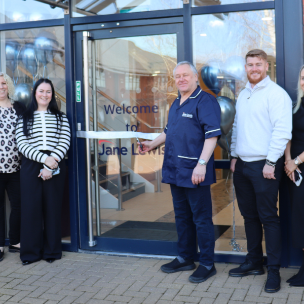 Male Jane Lewis Nurse cutting the ribbon to the new Jane Lewis North Wales office, with staff members around him.