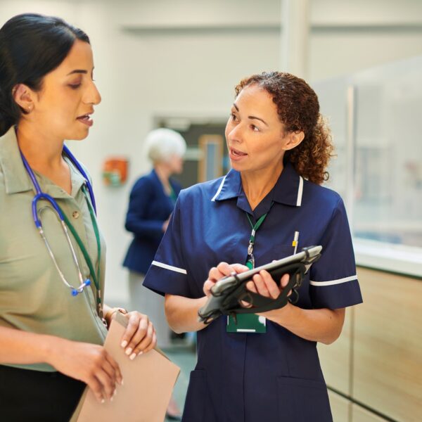 Female Nurse in navy blue uniform speaking to a female doctor next to a reception desk