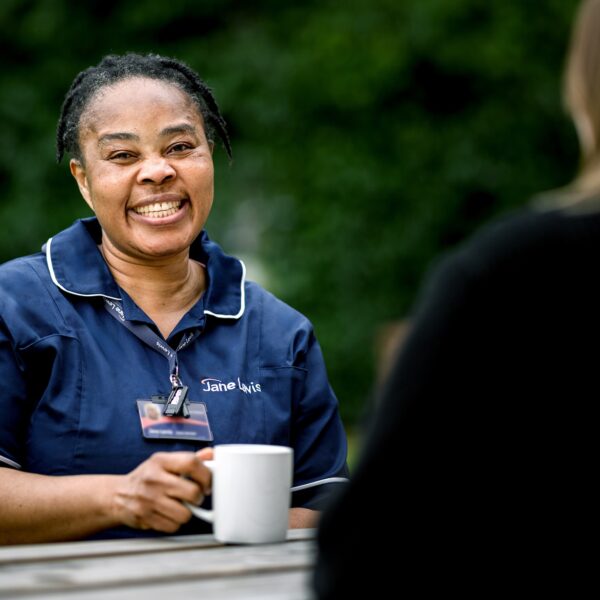 Nurse in a Jane Lewis uniform sitting on a picnic bench with a cup of tea