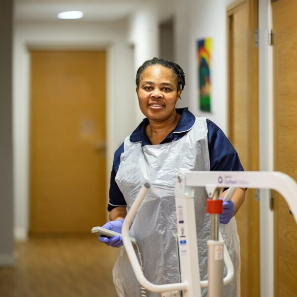 Female Jane Lewis Nurse in PPE moving a hoist in service corridor