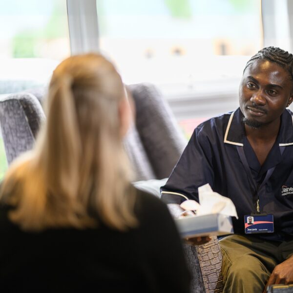 A male nurse in Jane Lewis uniform offering a female service user a tissue