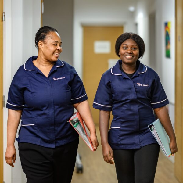Two female Jane Lewis nurses in uniform walking down a service corridor holding folders