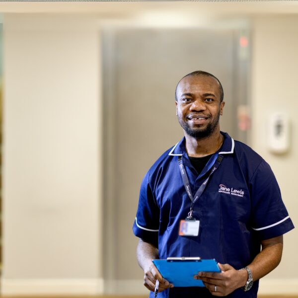 Male Jane Lewis Nurse standing in front of a lift with a blue clipboard in hand