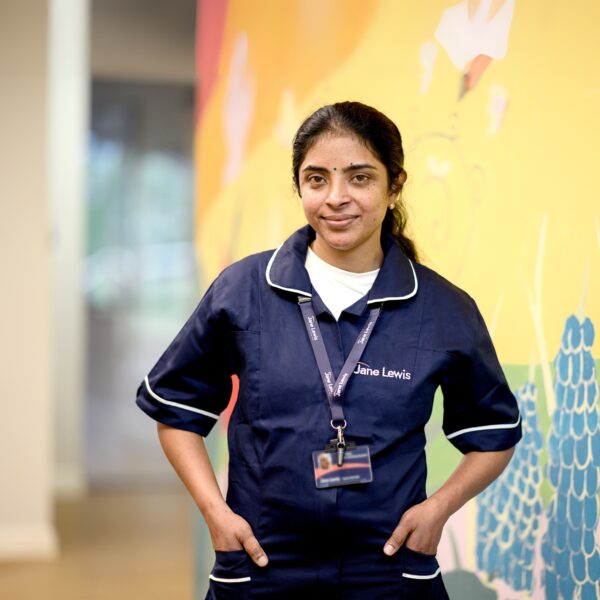 Female nurse, wearing a Jane Lewis navy blue, with her uniform standing in a bright service hallway