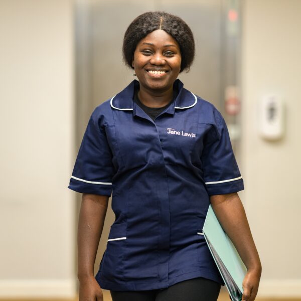 Female nurse in Jane Lewis uniform walking through the corridor in a service with a pale blue folder in hand