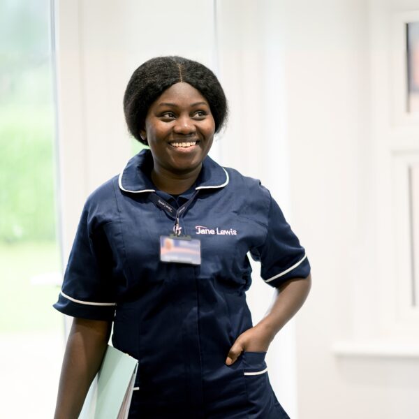 Female nurse in Jane Lewis uniform standing in front of patio doors holding a blue folder